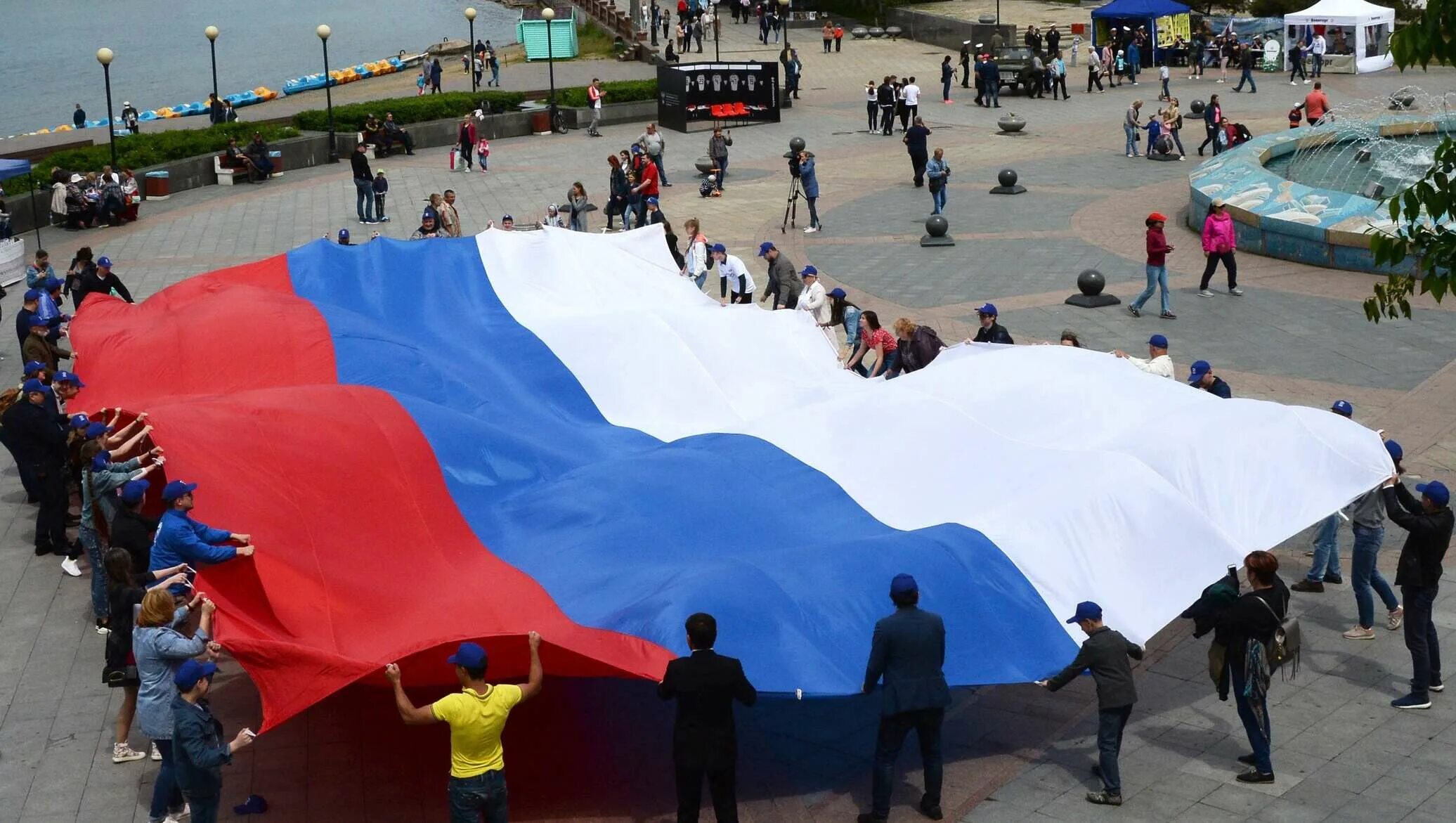 Страна сегодня отмечает. Самый большой флаг России. Празднование дня флага России. 12 Июня праздник. Люди с флагами России.