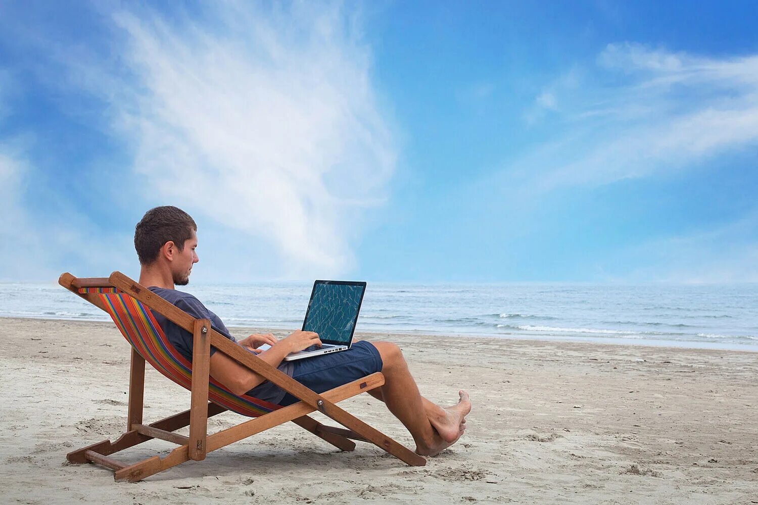 Человек с ноутбуком на пляже. Отдыхая трудимся. Человек на лежаке на пляже. Интересная работа. Человек отдыхает.