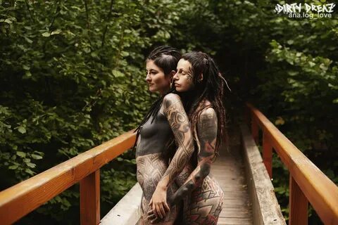 Heavily tattooed lesbians hold each other while totally naked on a bridge -...