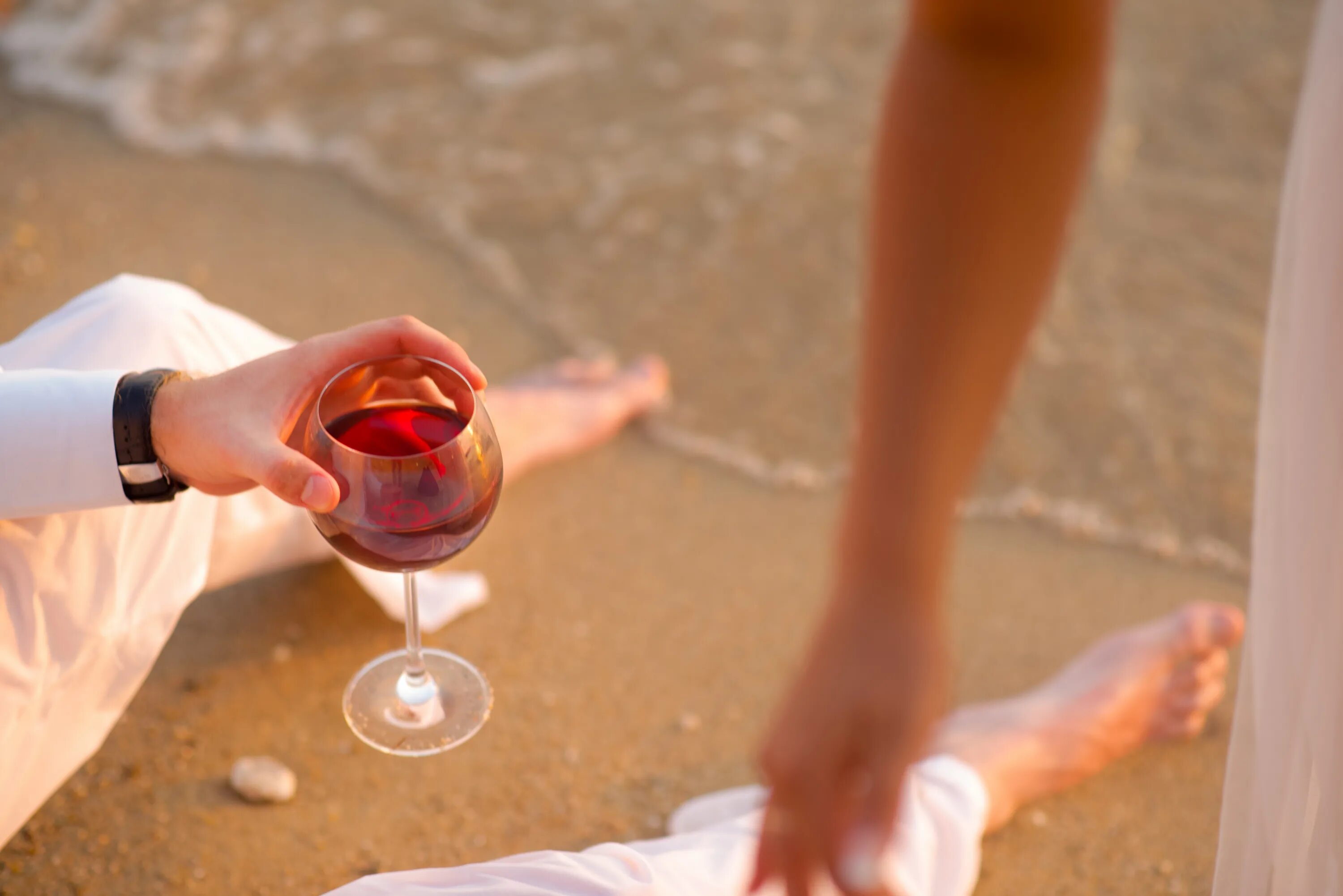 Порванное платье и бокал вина. Бокал вина на пляже. Рука с бокалом. Вино и море. Вино на песке.