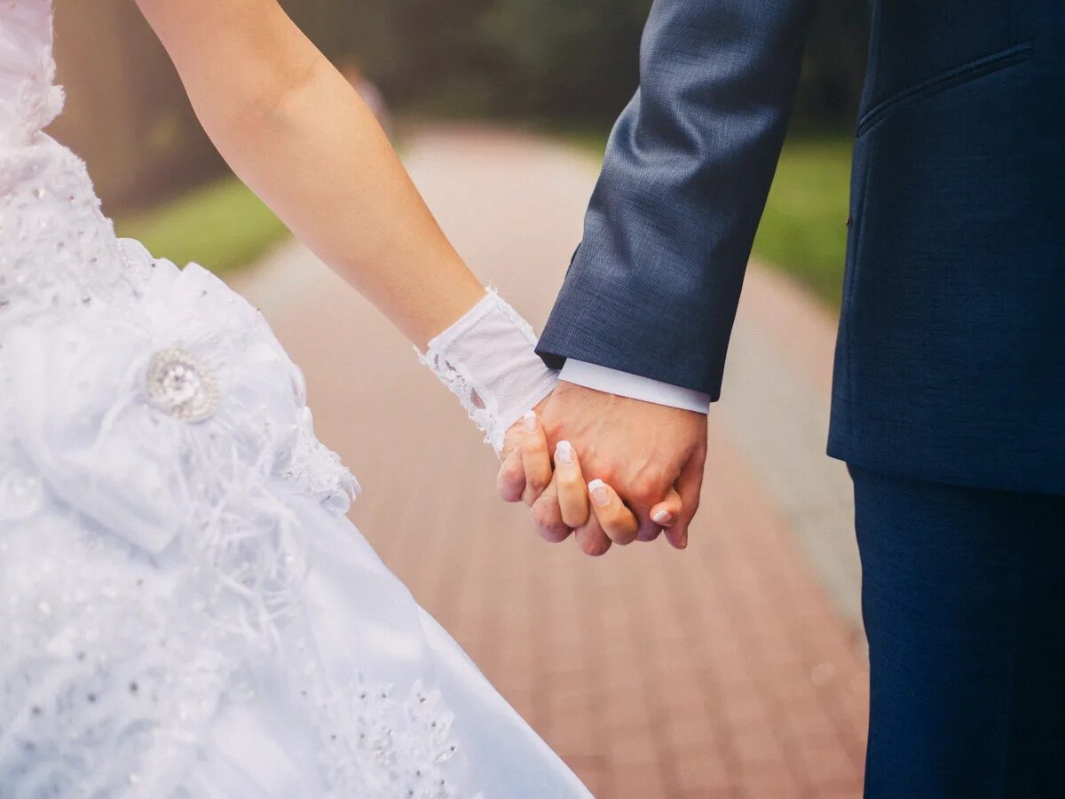 Опека брачный. Жених и невеста держатся за руки. Брак свадьба. Молодожены. Невеста на руках у жениха.