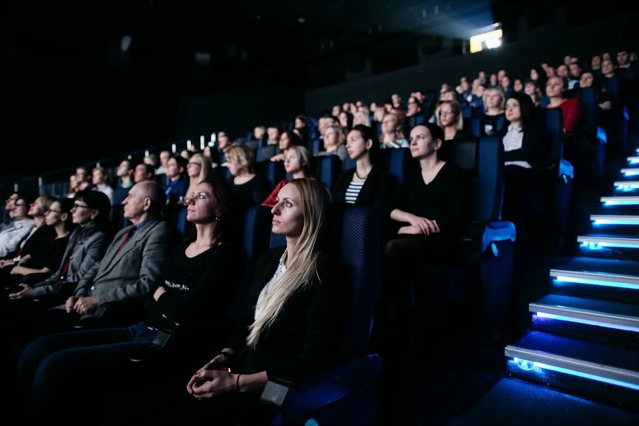 Кинофильмы прокат. Зрители в кинотеатре. Люди в кинотеатре. Полный зал людей. Зрители в кинозале.