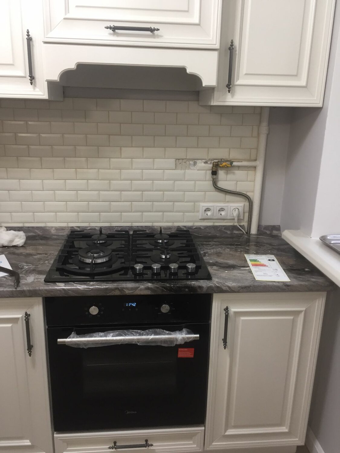 белая кухня с черной плитой, бытовая техника, варочная панель под газовой трубой, газовая труба и варочная панель, варочная панель